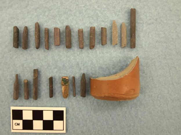 Photograph of fragmented objects on a gray backdrop next to a 10-centimeter scale, divided into one centimeter increments.