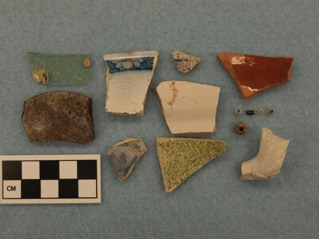 Photograph of fragmented objects on a gray backdrop next to a 10-centimeter scale, divided into one centimeter increments.