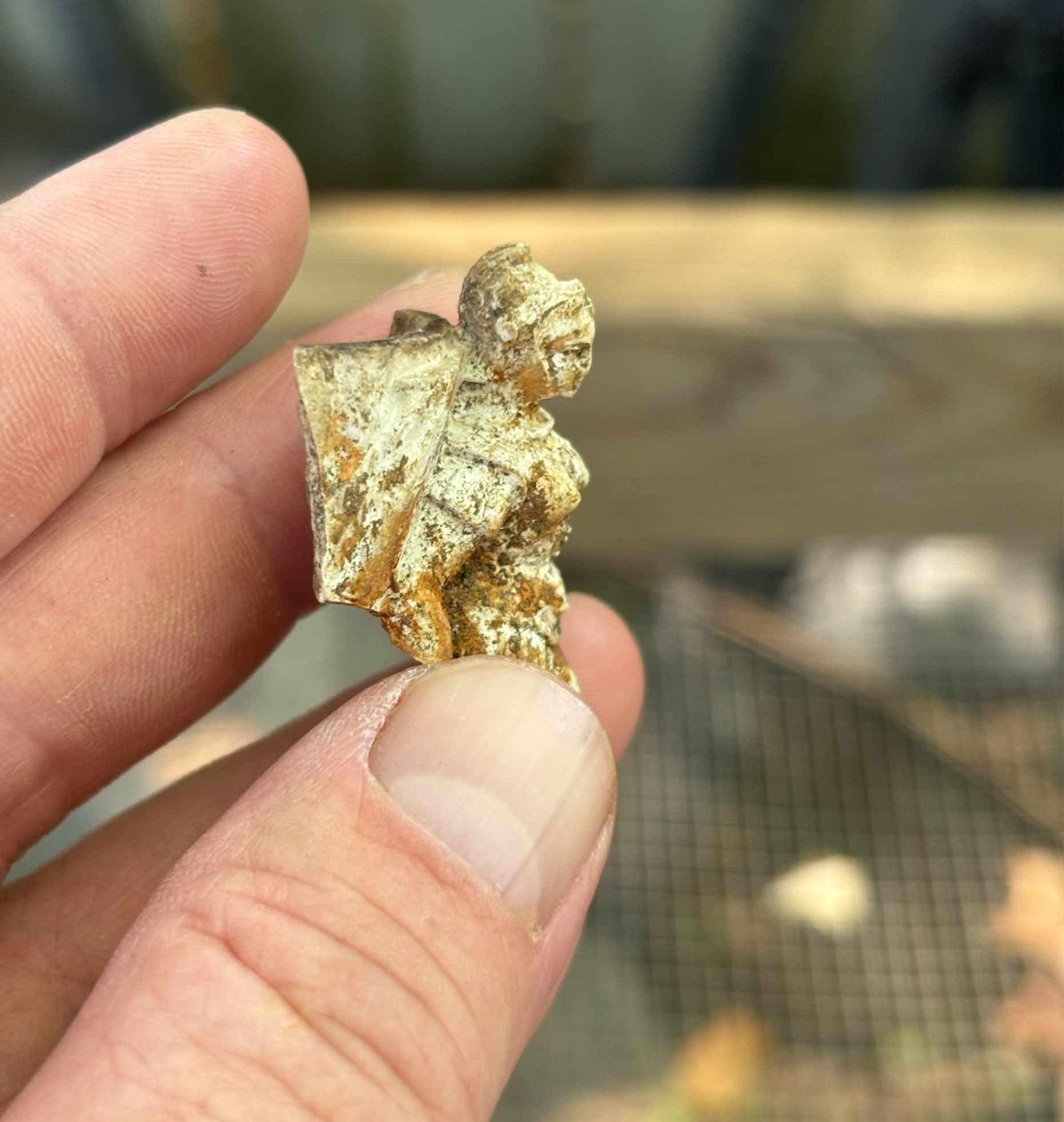 Photograph of a pipe molded in the image of a woman with a helmet, held between the fingers of an archaeologist.