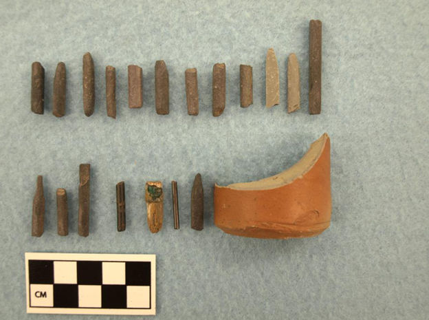 Photograph of fragmented objects on a gray backdrop next to a 10-centimeter scale, divided into one centimeter increments.