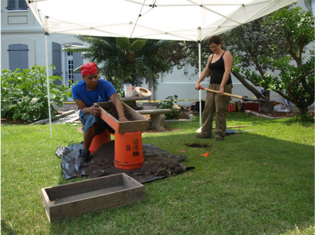 Photograph of students and volunteers excavating at The Old Usruline Convent. They are digging with shovels and screening dirt through mesh screens under a tent.