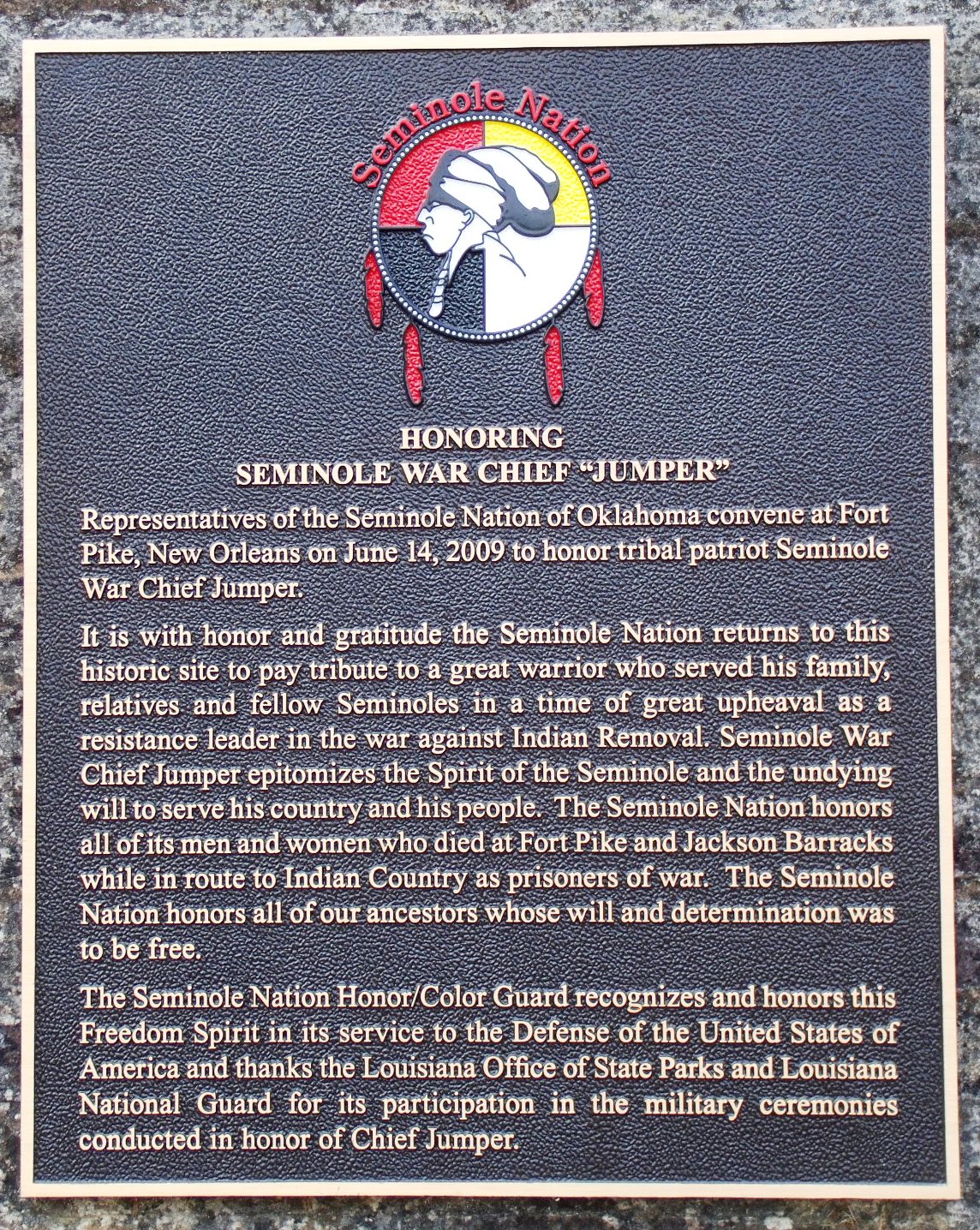 Photo of a metal plaque with a circular seal at the top in the colors white, black, red and yellow.