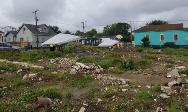 Photograph of an urban city block covered with building debris. Archaeologists are working under white tents.