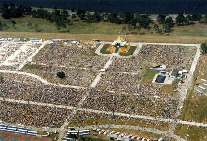 Aerial shot of a large field full of people, with a yellow and white tent at one end.